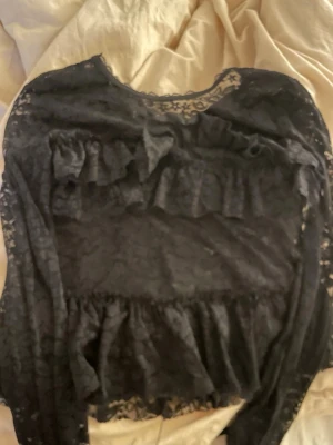 Svart spetsblus med volanger från Nelly - Säljer en svart långärmad spetsblus från Nelly med volangdetaljer framtill och längs ärmarna. Blusen är i väldigt bra skick, använd typ 2 gånger. Den har även knyte i nacken vilket gör det till en fin detalj. Storlek S, hör av dig vid frågor! (Inte så bra bilder pga min backkamera är sönder!)