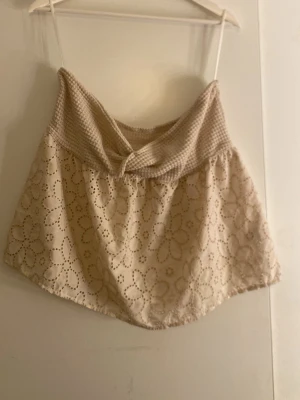 Beige broderad topp - Söt beige topp med broderade blommor. Överdelen har ett ribbat, småmönstrat tyg och en twistad detalj framtill. Perfekt för varma dagar och ger en romantisk vibe.