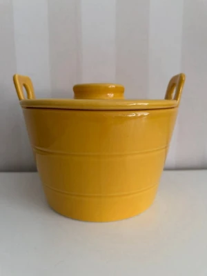 Gul keramikgryta med lock retro 80 tal - Säljer en rund gul keramikgryta med lock och två handtag. Grytan har en blank yta och locket har ett litet hål för ånga. Perfekt för servering eller dekoration i köket.En gul keramikgryta med lock. Grytan har handtag på sidorna och locket har en skåra för en sked eller slev. Perfekt för servering eller förvaring.  ?? Bedårande och originell liten gryta eller kompottform från 1980-talet i handgjord vitrokeramik, • vacker färg ?? Summer Sun eller Saffron (gul-orange). • Perfekt för bakning och för