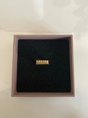 Guldfärgad Edblad ring med MOM-text - Snygg guldfärgad ring med texten MOM i blockbokstäver. Ringen har en stilren och modern design med rektangulär form på textplattan. Perfekt som present till mamma eller för att visa uppskattning. 