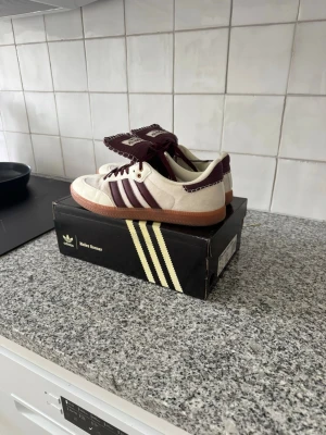 Adidas Wales Bonner sneakers vita/vinröda - Kvitto och låda finns! Använda fåtal gånger. Snygga Adidas Wales Bonner sneakers i vitt och vinrött med klassiska tre ränder på sidan. Skorna har lågt skaft, gummisula och detaljer i mocka och läder. Perfekta för dig som gillar stilrena och trendiga sneakers med unik design. 