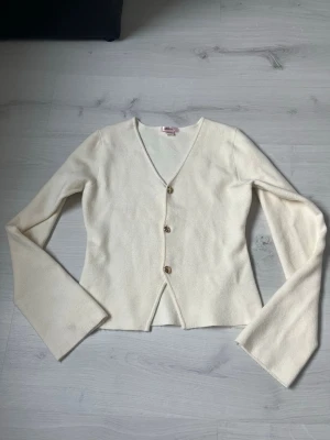 Topp - Elegant och tidlös finstickad tröja med knappar i guld och lätt urringning. 