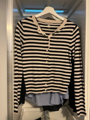 Randig svartvit kofta med knappar - Snygg kofta med svarta och vita horisontella ränder och knäppning framtill. Långärmad modell med rund halsringning och ribbade muddar. Perfekt att slänga över en t-shirt eller skjorta för en avslappnad look.