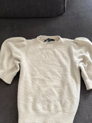 Beige stickad tröja Vero Moda - Trendig beige stickad tröja från Vero Moda med puffärmar och ribbade muddar. Tröjan har rund halsringning och är gjord i ett mjukt, mysigt material som passar perfekt till höst och vinter. Enkel att styla med både jeans och kjol.