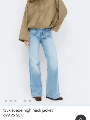 Beige faux mockajjacka med hög krage - Snygg ljusgrön jacka i faux mocka med hög krage och vida ärmar. Jackan har dragkedja framtill och en loose passform som ger en avslappnad look. Perfekt för dig som gillar trendiga och bekväma plagg.