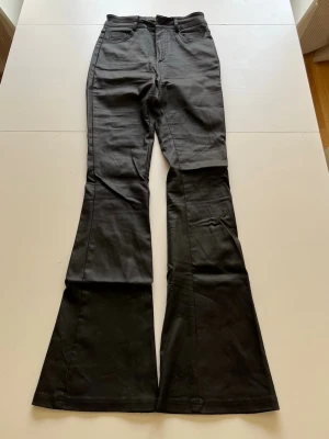 Svarta läder bootcut med utsvängda ben - Säljer ett par svarta läder bootcut  med riktigt utsvängda ben. Byxorna har klassisk femficksdesign och normal passform upptill. Perfekta för dig som vill sticka ut med en retroinspirerad look.