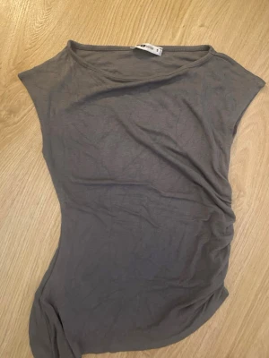 Grå ärmlös topp från new yorker - Säljer en enkel grå ärmlös topp från H&M med rund halsringning och rynkade detaljer på sidan. Toppen har en slim passform och är tillverkad i mjuk bomull, perfekt att styla till olika outfits. köpt på new yorker aldrig använd