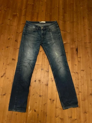Dressman raka jeans med slitningar - Säljer ett par blå dressman jeans med raka ben och snygga slitningar på framsidan. Jättefin wash, slitningar limmade med jeanslapp, funkar fint. Storlekslappen borta, passar 175-185 lång ungefär. Jag är 68 kg 185 cm för uppskattning. Skulle tippa 30W 32L. Vid frågor eller funderingar, skicka ett DM! Mvh Oskar