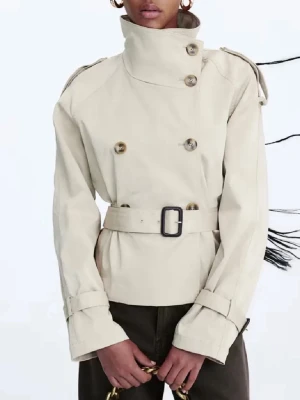 Beige kort trenchcoat med bälte - Stilren beige trenchcoat med hög krage, dubbelknäppning och bälte i midjan. Jackan har axelklaffar, stora knappar och justerbara ärmslut. Perfekt för dig som gillar klassisk men modern stil.
