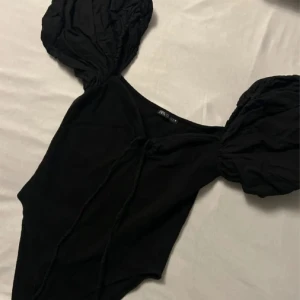 Svart body med puffärmar - Trendig svart body från NA-KD med stora puffärmar och djup urringning. Tillverkad i mjukt och stretchigt material som sitter snyggt på kroppen. Perfekt för dig som vill ha en statement-piece i garderoben.