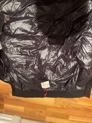 Svart jacka från Moncler  - Snygg svart jackafrån Moncler glansigt yttertyg och diskret dragkedja. Västen har en modern look och är perfekt för lager-på-lager-stil. Tillverkad i lätt och värmande material med dunfyllning.