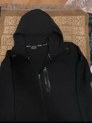 Dry Tex Tech Full Zip Hooded Jacka – Svart - ✔️ Hel dragkedja framtill ✔️ Med huva ✔️ Färg: Svart ✔️ Storlek: L ✔️ Stilren och bekväm design   #jacka #hoodie #sportjacka #träningsjacka #drytex #svartjacka #fullzip #unisex #streetwear #sportstyle #vardagskläder