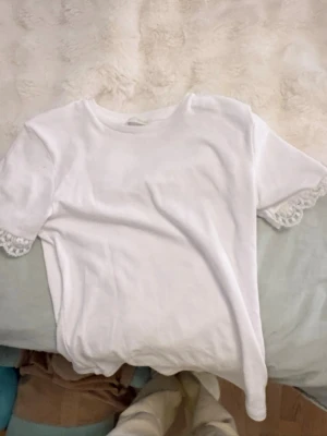 Vit t-shirt med spetsdetalj - Säljer en vit t-shirt med korta ärmar och snygga spetsdetaljer vid ärmsluten. Enkel och clean design som passar till det mesta. Tillverkad i mjukt material för skön känsla hela dagen. Säljer båda för 250 men en för 190. Används aldrig