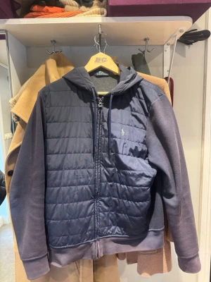 Mörkblå Polo Ralph Lauren cardigan  - Snygg mörkblå cardigan från Polo Ralph Lauren med quiltad front, dragkedja och broderad logga på bröstet. Jackan har huva och mjuka ärmar i sweatshirtmaterial, perfekt för lager på lager under höst och vår. Vid snabbt köp kan jag gå ner i pris 