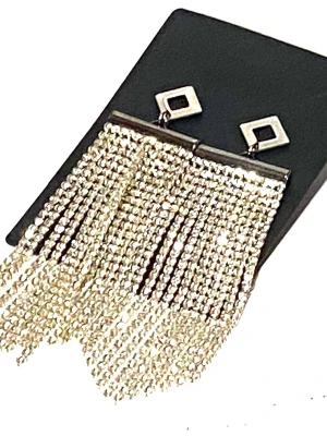 Silvriga statement örhängen med strass - Glittriga örhängen i silverfärg med fyrkantig topp och långa fransar av strass. Örhängena har en modern, geometrisk design och ger en riktigt lyxig känsla. Perfekta för dig som vill sticka ut och addera extra bling till din look. Längd 10.5cm. Bred 2.5cm 