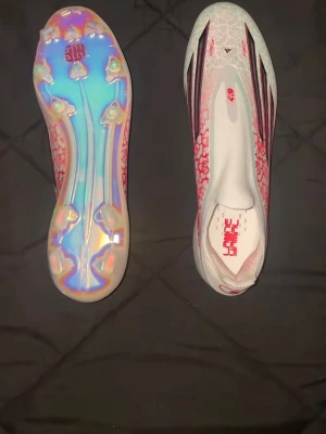 Adidas X Speedportal fotbollsskor - Säljer ett par Adidas X Speedportal fotbollsskor i vitt med röda och svarta detaljer. Skorna har en futuristisk design med mönstrad ovandel och iriserande sula. Lätta material och strömlinjeformad form för maxad speed på planen. Perfekta för dig som vill sticka ut!