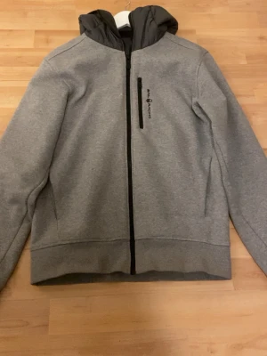 Grå jacka från Sail Racing - Snygg grå jacka från Sail racing med svart dragkedja och bröstficka. Jackan har huva och är helfodrad med quiltad insida. Perfekt för kyligare dagar och har en stilren, sportig look. Pris kan diskuteras men nypris ligger på ca 1500