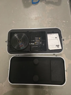 DJ Hero handkontroll med väska till wii  - Säljer en DJ Hero handkontroll till spelkonsol, komplett med original väska, manual och DJ Hero-spel till Wii. Handkontrollen är svart med färgade knappar och har en rund skivtallrik i plast. Perfekt för musikspel och partyspel.