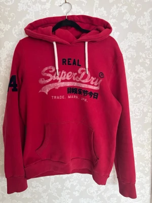 Röd superdry hoodie - Säljer en fet och bekväm Superdry hoodie i storlek: M🤩Hoodien har en snygg röd färg♦️Det finns en liten fläck som syns på bilderna går troligen att tvätta bort men har inte testat😁Priset är förhandlingsbart så skicka gärna prisförslag☺️