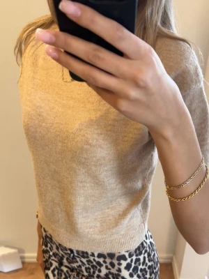 Beige stickad kortärmad tröja - Säljer en beige stickad tröja med korta ärmar och rund hals. Tröjan har en mjuk och tunn stickning, perfekt för lager på lager. Säljer kjolen separat🩷