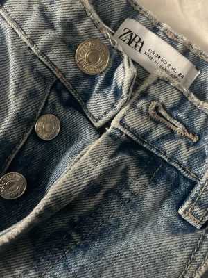 Ljusblå raka jeans från Zara - Säljer ett par ljusblå jeans från Zara med raka ben och klassisk femficksmodell. Jeansen har knäppning med silverfärgade knappar och är gjorda i slitstarkt denimtyg. Perfekta för en avslappnad och trendig look.💙💙💙