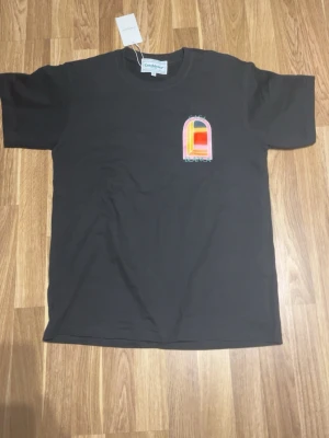 Svart t-shirt från Casablanca - Svart t-shirt från Casablanca med färgglatt grafiskt tryck fram och stort tryck med texten 'Casa Blanca' på ryggen. Klassisk passform och rund hals. Perfekt för dig som gillar streetwear och unika prints.