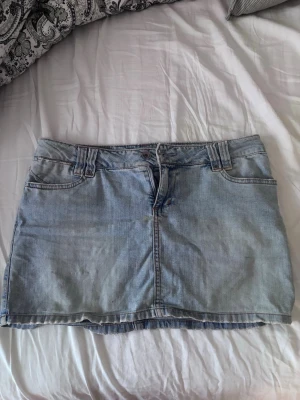 Ljusblå jeanskjol från Only - Trendig ljusblå jeanskjol från Only med klassisk femficksdesign, bälteshällor och knappgylf. Kjolen har en kort passform och är perfekt för en avslappnad och cool stil. Passar till allt från sneakers till boots.