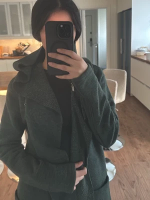 Mörkgrön lång kappa med huva - Säljer en mörkgrön kappa med stor huva. Kappan har stora fickor och är tillverkad i ett tjock, mjukt material som passar perfekt när det är lite kyligt ute. 