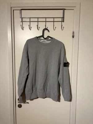 Stone Island sweatshirt  - Säljer en grå sweatshirt från Stone Island med klassisk rund hals och ribbade muddar. Tröjan har den ikoniska Stone Island patchen på vänster ärm och är tillverkad i mjukt bomullsmaterial. Perfekt för dig som gillar stilrena och trendiga plagg.