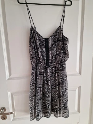 Svartvit mönstrad kort klänning Bikbok - Säljer en svartvit kort klänning med tunna axelband och mönster. Klänningen har en lätt och luftig passform, resår i midjan som framhäver midja. Luftig tyg och underklänning.
