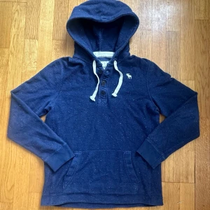 Mörkblå Vintage Hoodie från Abercrombie and Fitch🤩(sällsynt) - En supersnygg hoodie i vintage/archive stil från märket Abercrombie & Fitch! Hoodies har 3 knappar närmare kragen som är något som de flesta letar efter på en sådan hoodie🤩Superfint skick utan några skador alls, och passar suveränt nu under de lite kallare månaderna❄️Denna modellen är mycket eftertraktad och sällsynt. Bara att fråga om du undrar något🤝 Storlek S på etiketten men passar närmare storlek M👍