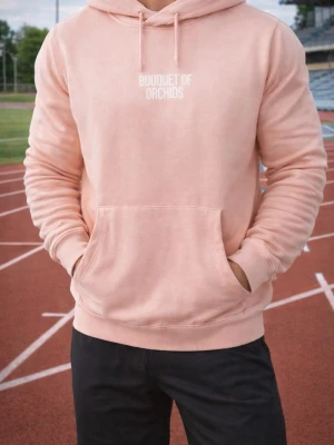 Ljusrosa hoodie Bouquet of Orchids - Ljusrosa hoodie med vit text 'Bouquet of Orchids' på bröstet och en stor abstrakt konstbild i orange och svart på ryggen. Klassisk känguruficka framtill och justerbar huva med dragsko. Mjuk bomullsblandning för skön känsla.