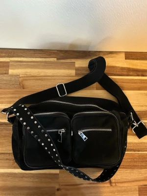 Svart axelväska från Noella - Svart väska från Noella i modellen Celia. Väskan är 20x32x10 cm och har två fickor på utsidan, samt ett huvudfack med innerfickor. Dustbag (orginalförpackning) medföljer. Nypris är 849 kr, jag säljer för 500 kr 💕