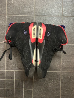 Svarta Air Jordan Mvp Retro sneakers - Säljer ett par Air Jordan Mvp Retro sneakers i svart mocka med röda och lila detaljer. Skorna har högt skaft, synlig Air-sula och klassiska perforeringar på sidorna. Ikoniska Jumpman-loggan på plösen och färgade accenter längs sulan och hälen. Smutsen finns inte