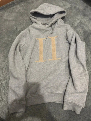 Les deux hoodie - Snygg grå hoodie med stor beige romersk siffra II på bröstet. Hoodien har huva med dragsko och ribbade muddar vid ärmar och nederkant. Perfekt för en avslappnad och trendig look.