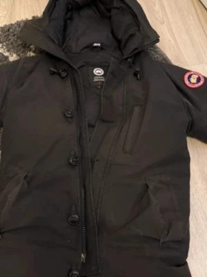 Kom med prisförslag eller byte mot en skön cardian Svart dunjacka från Canada Goose - Säljer en svart dunjacka från Canada Goose med huva och stora knappar framtill. Jackan har tre fickor, varav en bröstficka med dragkedja och två sidofickor. Klassisk patch på ärmen och varm vaddering i dun. Perfekt för kalla vinterdagar.