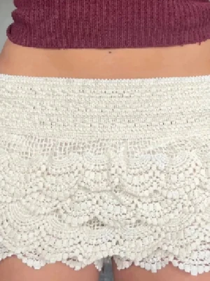 Beige spetsshorts med volanger - Säljer ett par vita virkade shorts med flera lager volangdetaljer. De har hög midja och ett elastiskt midjeband för skön passform. Perfekta till sommaren för en söt och bohemisk look.