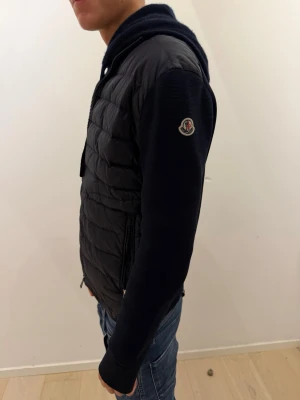 Moncler cardigan tricot - Säljer en svart pufferjacka från Moncler med quiltad front och stickade ärmar. Jackan har dragkedja framtill, två sidofickor med dragkedja och Moncler-logga på ärmen. Perfekt för kalla dagar och riktigt snygg till jeans. Köpt från luisaviaroma för runt 10 tusen. Kvitto finns på Mail så såklart äkta. Hör av dig vid frågor. 🙌