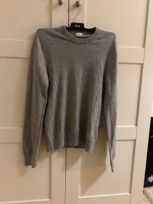 Grå stickad tröja från Filippa k - En stilren grå stickad tröja från Filippa K med rund halsringning och långa ärmar. Tröjan är tunnstickad och har ribbade muddar vid ärmslut och nederkant. Perfekt för lager på lager och enkel att matcha med olika outfits. Använd fåtal gånger.