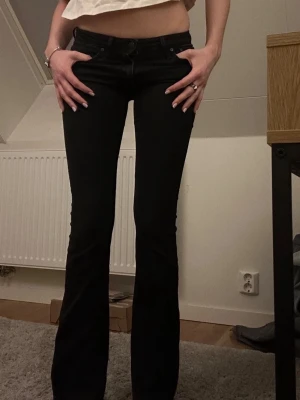 Svarta low waist bootcut jeans - Snygga svarta bootcut jeans med klassisk femficksmodell och låg midja. Jeansen har en lätt utsvängd passform nedtill och är tillverkade i ett mjukt denimtyg som sitter skönt. Perfekta för en trendig och avslappnad look. Storlek: W26 L30