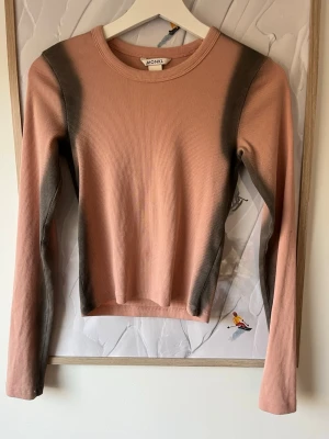 Rosa ribbad långärmad topp Monki - Trendig långärmad topp från Monki i ljusrosa med mörkgrå detaljer längs sidorna och ärmarna. Ribbad struktur och rund halsringning ger en snygg och bekväm look. Perfekt att styla med jeans eller kjol för en cool vardagsoutfit.