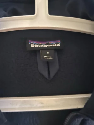 Mörkblå fleecejacka från Patagonia - Mysig mörkblå fleecejacka från Patagonia med hel dragkedja framtill och två fickor med dragkedja. Jackan har hög krage och är perfekt för lager-på-lager. Klassisk logga på bröstet och mjukt material som håller värmen. Perfekt nu för våren! Pris går att diskuteras vid snabb affär 