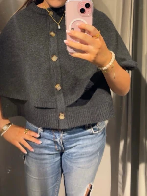 Mörkgrå stickad cape med knappar - Snygg mörkgrå stickad cape tröja från Zara. Använd ett fåtal gånger! 