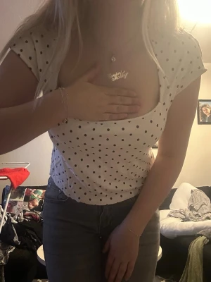 Vit prickig topp med fyrkantig urringning - Snygg vit topp med svarta prickaror och fyrkantig urringning. Kortärmad modell i mjuktult bomullsmaterial, perfekt till jeans eller kjol. Trendig och enkel att styla för en fräsch look.