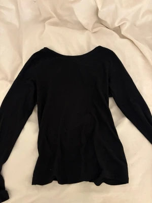 Svart långärmad topp i bomull - En enkel och stilren svart långärmad topp med rund halsringning. Perfekt att matcha med jeans eller kjol. Materialet känns mjukt och bekvämt, troligtvis bomull. Passformen är normal och toppen är utan mönster eller detaljer. Passar xs och M