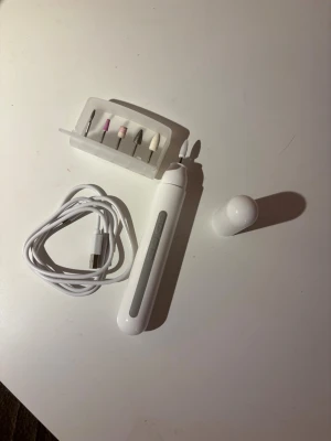 Elektrisk nagelfil med tillbehör - Elektrisk nagelfil i vitt med flera sliphuvuden för olika nagelbehandlingar. Inkluderar USB-laddningskabel och skyddshölje. Perfekt för att forma, slipa och polera naglar hemma. Kompakt och smidig design, passar både manikyr och pedikyr.köptes nyligen på Clas Ohlson för 399kr.