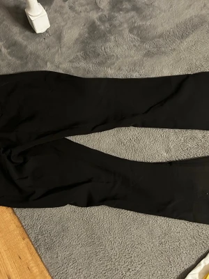 Svarta bootcut-byxor - Säljer ett par svarta bootcut-byxor med hög midja och utsvängda ben. Byxorna har knapp- och dragkedjestängning framtill och är tillverkade i ett stretchigt material för skön passform. Perfekta för dig som gillar en stilren och enkel look.