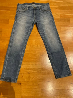 Blå raka jeans från Lee - Snygga blå jeans från Lee med raka ben och klassisk femficksdesign. Jeansen har en lätt tvättad look med slitningar framtill och Lee-logga på bakfickan. Perfekta till en avslappnad stil. Materialet är denim i bomull. Stolek w33 L32