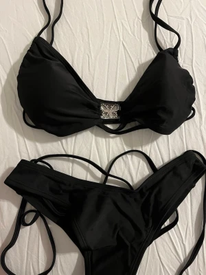 NY! Y2K mcbling stil Svart bikini med strass fjäril  - Snygg svart bikini med tunna band och strassdetalj framtill på överdelen. Både över- och underdel har flera smala band som ger en trendig look. Perfekt för stranden eller poolen. Materialet känns mjukt och följsamt.