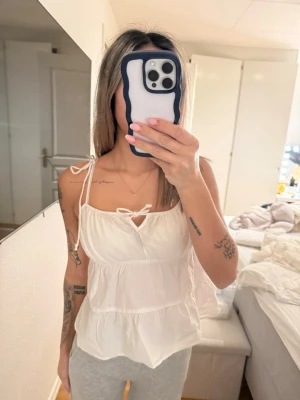 Vit linnetopp med knytband - Säljer en söt vit linnetopp med tunna axelband och knytband både fram och på axlarna. Toppen har volangdetaljer och är ärmlös, perfekt för en avslappnad och trendig look. Materialet känns lätt och luftigt. Storlek 38 men skulle säga mer som 34/36